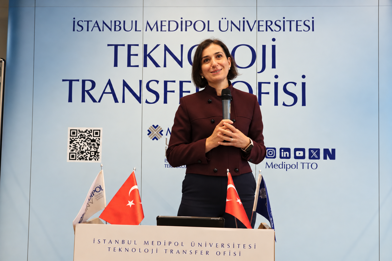 Woman speaking at podium with flags